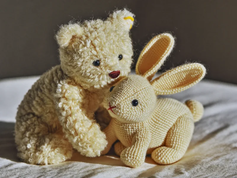 Ourson en peluche et lapin tricoté posés sur un plaid en lin